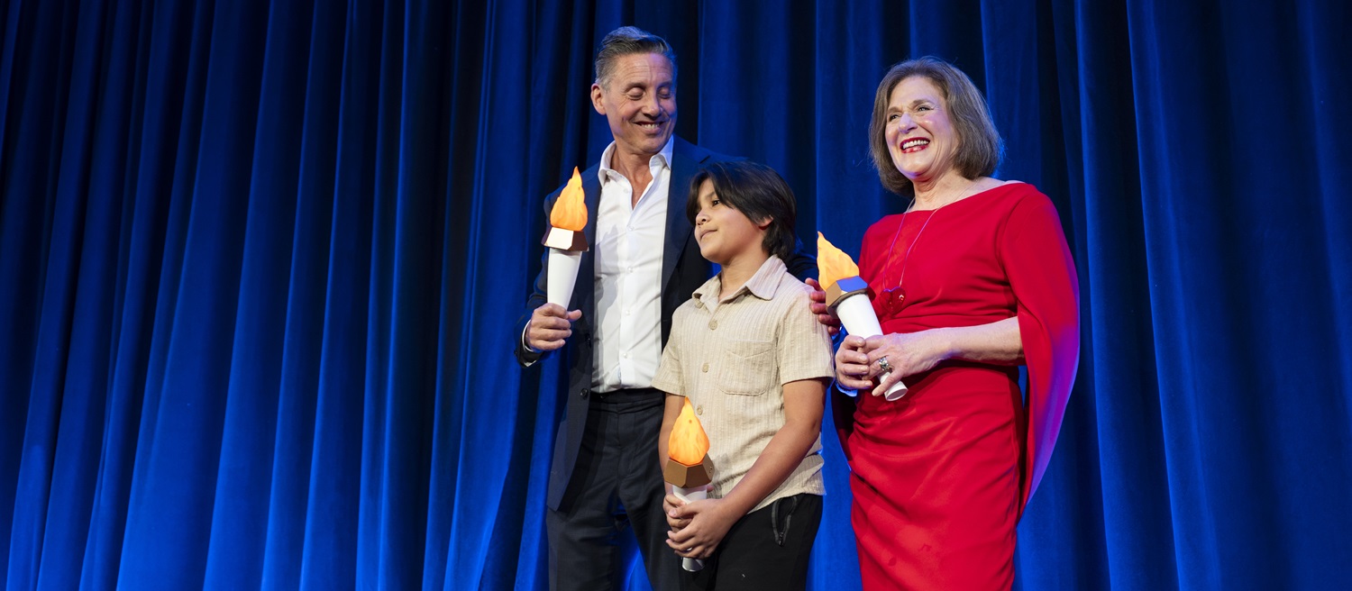 Man, woman, and child on stage holding mock torches.